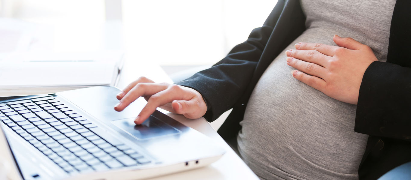 Eine schwangere Frau sitzt vor dem Laptop.