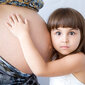 Ein Mädchen hört in den Babybauch der Mutter.