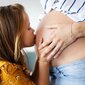 Ein Mädchen küsst den Babybauch ihrer Mutter.