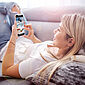 Eine Frau liegt mit ihrem Smartphone auf dem Sofa.